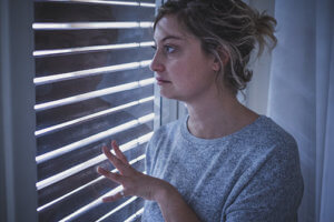 A woman participating in anorexia treatment programs for women peers out of a window through some blinds